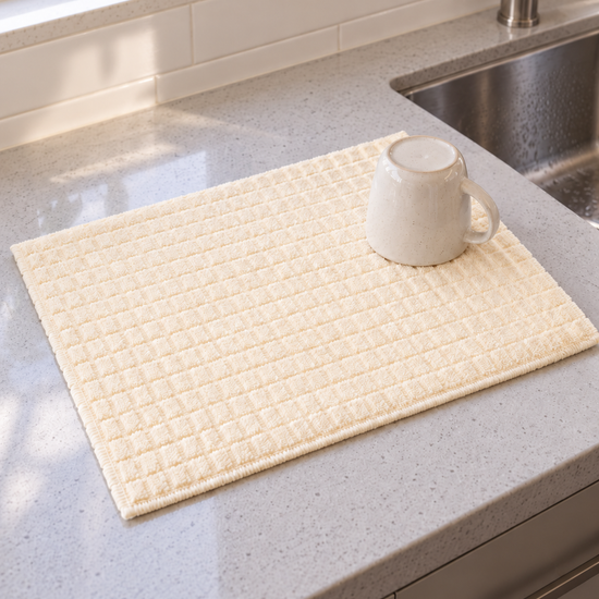 T&CO absorbent waffle-weave microfiber kitchen dish drying mat in cream ivory beside stainless steel sink with ceramic mug