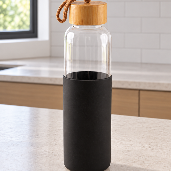 T&CO clear borosilicate glass water bottle with protective black silicone sleeve, natural bamboo lid, and braided carry strap