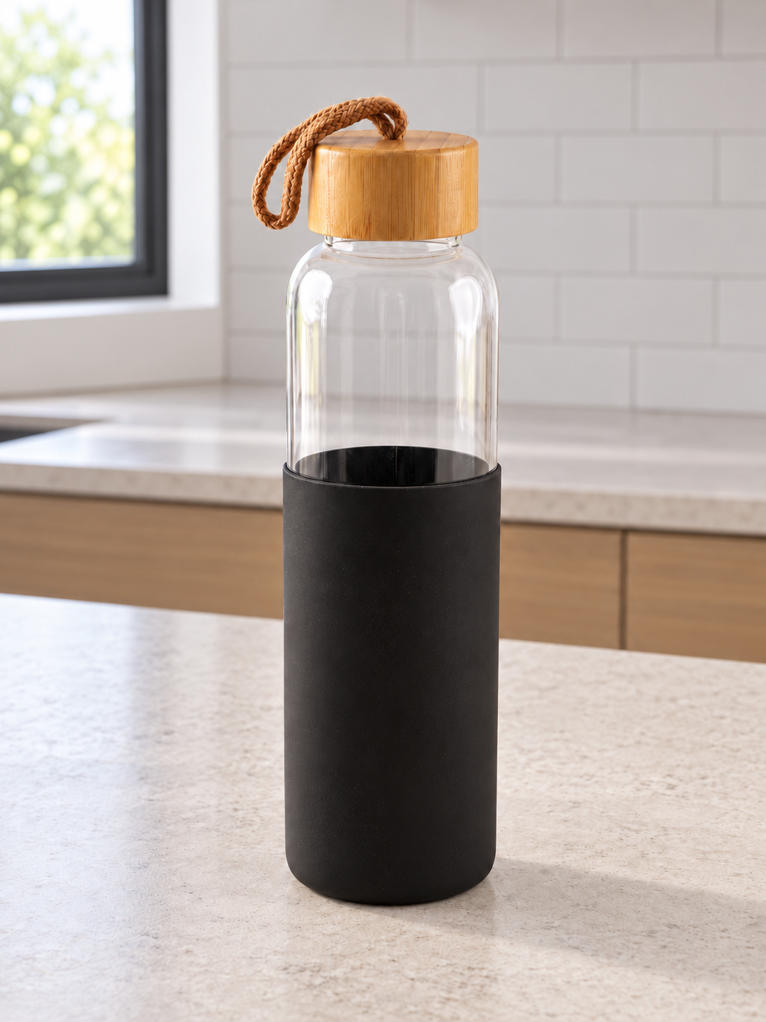 T&CO clear borosilicate glass water bottle with protective black silicone sleeve, natural bamboo lid, and braided carry strap