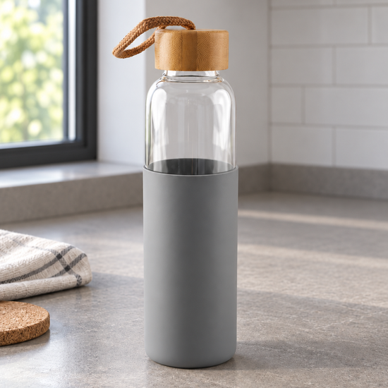 T&CO clear borosilicate glass water bottle with stone grey silicone sleeve, natural bamboo lid, and braided carry cord