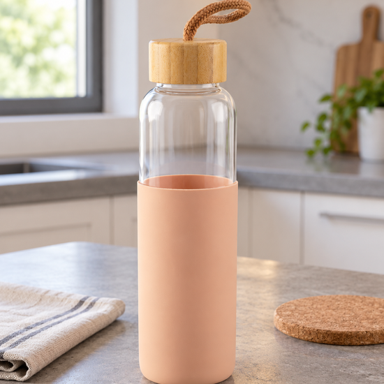 T&CO clear borosilicate glass water bottle encased in peach pink protective silicone sleeve with natural bamboo lid and carry strap