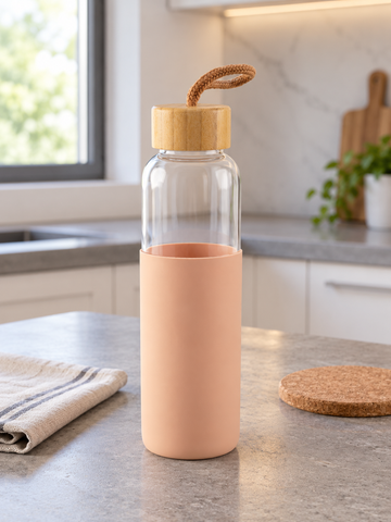 T&CO clear borosilicate glass water bottle encased in peach pink protective silicone sleeve with natural bamboo lid and carry strap
