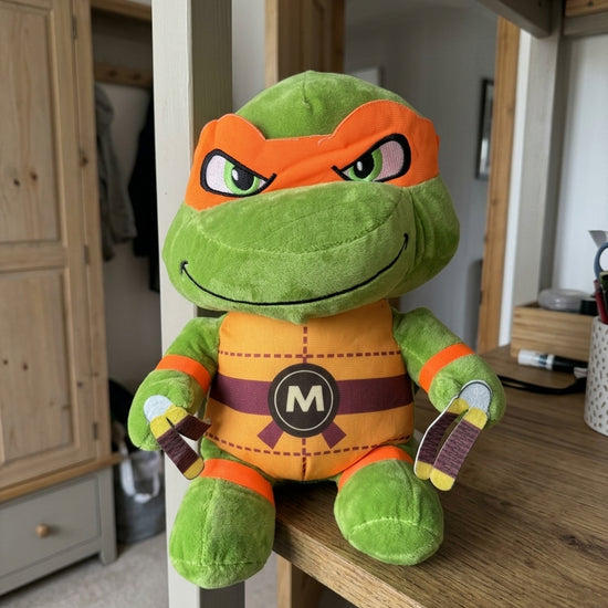 T&CO TMNT Ninja Turtle Michelangelo plush toy with orange eye mask, 'M' belt buckle, and twin nunchucks (31cm)