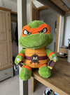 T&CO TMNT Ninja Turtle Michelangelo plush toy with orange eye mask, 'M' belt buckle, and twin nunchucks (31cm)