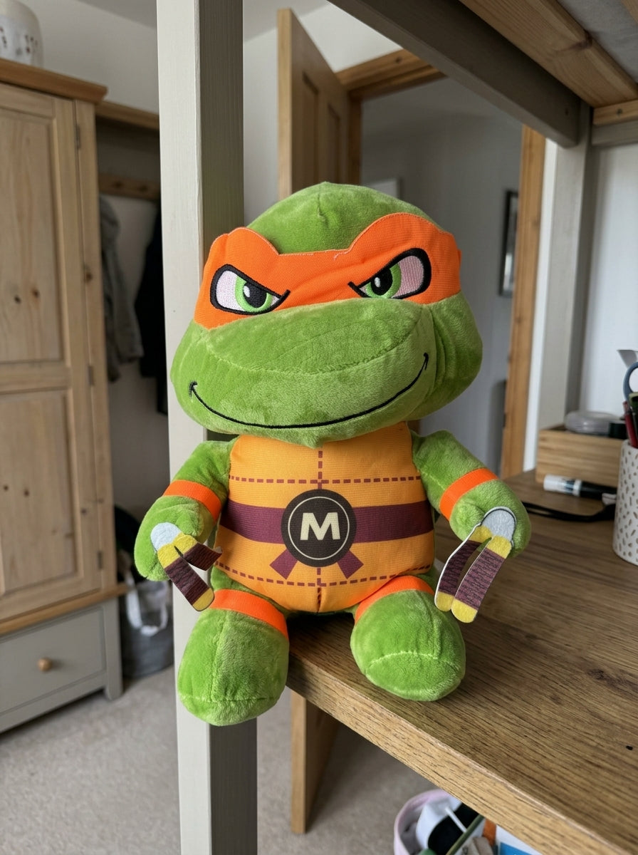 T&CO TMNT Ninja Turtle Michelangelo plush toy with orange eye mask, 'M' belt buckle, and twin nunchucks (31cm)