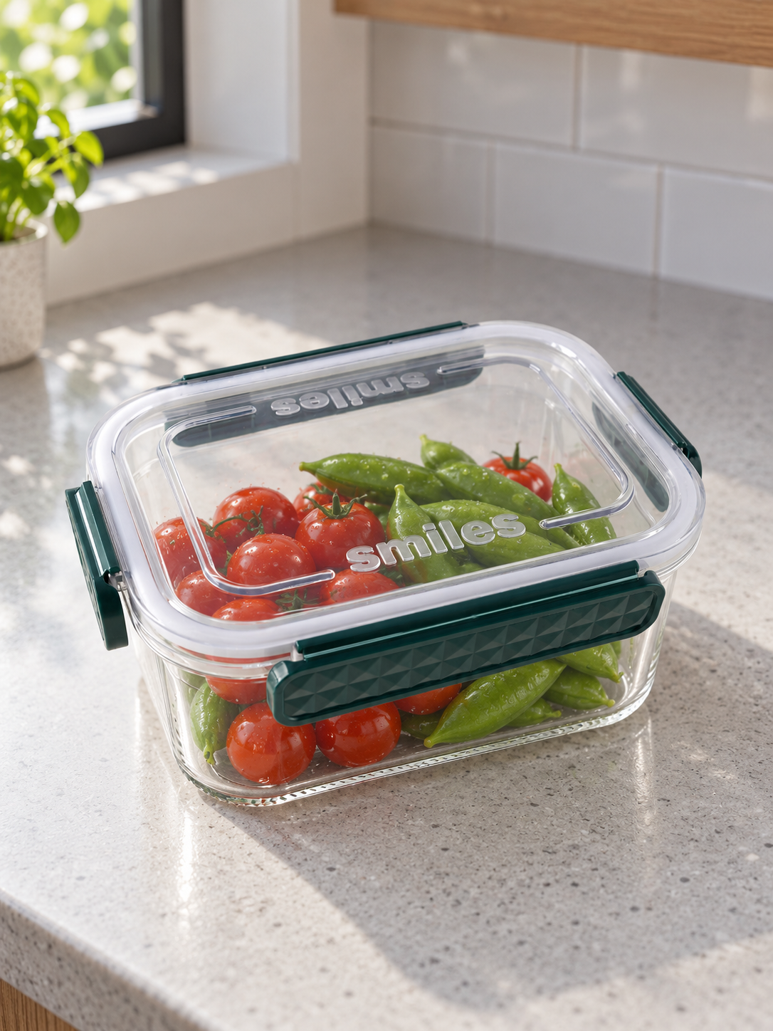 T&CO Smiles airtight clear food storage container with emerald green locking latches filled with fresh cherry tomatoes and snap peas