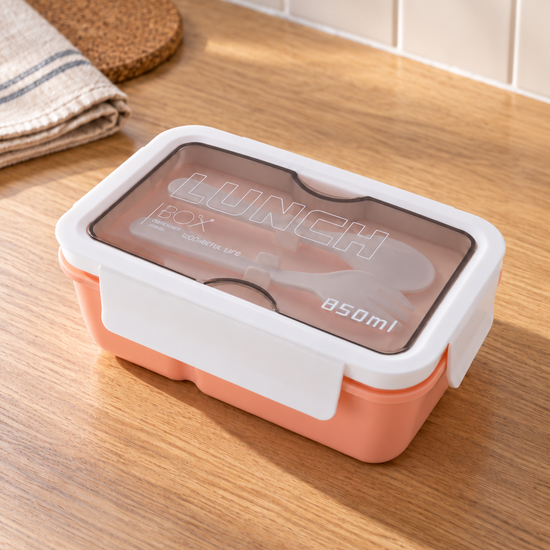 T&CO 850ml bento lunch box in warm peach coral with white clip lock lid and top smoked compartment containing reusable fork and spoon