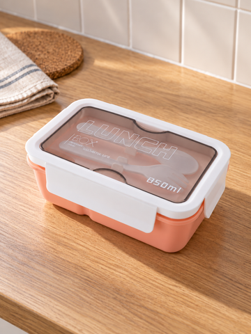 T&CO 850ml bento lunch box in warm peach coral with white clip lock lid and top smoked compartment containing reusable fork and spoon