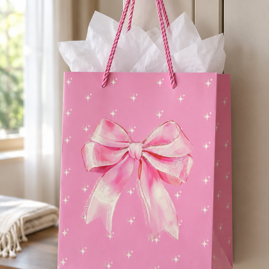 Small vibrant pink gift bag featuring an oversized glittery pink ribbon bow centerpiece, starbursts, and pink braided rope handles