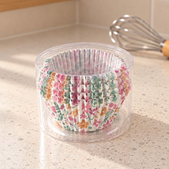 T & CO clear cylindrical pack of fluted paper cupcake baking liners featuring vibrant floral blossom print with pink and yellow flowers on kitchen countertop