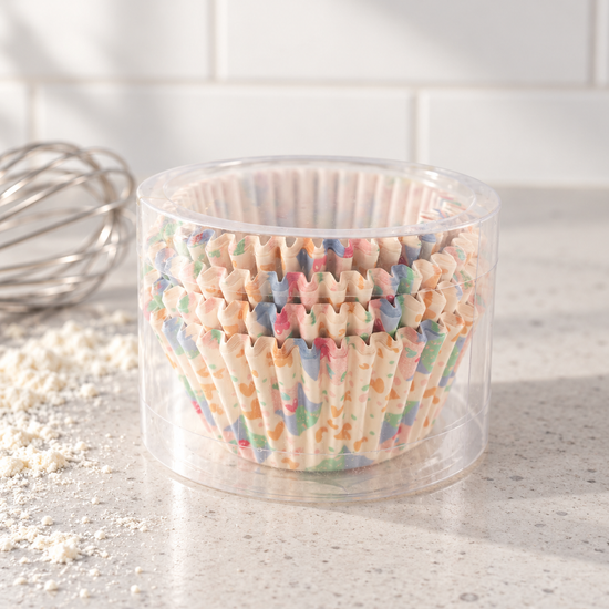 T & CO clear cylindrical pack of fluted paper cupcake baking cases featuring cheerful pastel terrazzo confetti print on modern kitchen counter