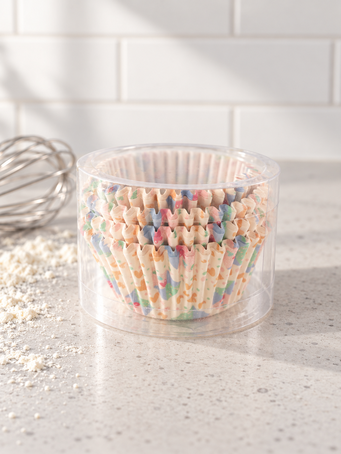 T & CO clear cylindrical pack of fluted paper cupcake baking cases featuring cheerful pastel terrazzo confetti print on modern kitchen counter