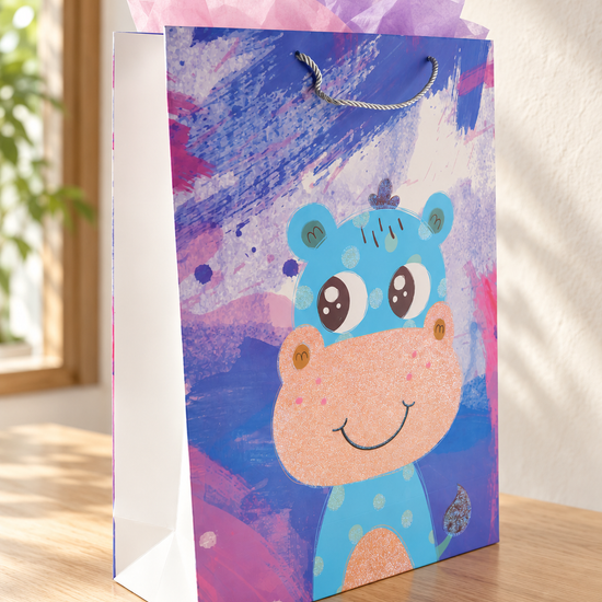 Hippo Joy extra large kids paper gift bag featuring a friendly blue cartoon hippo with glitter accents and peach snout on a painterly sky blue background with silver rope handles
