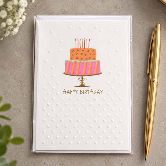 Embossed Happy Birthday greeting card featuring a two-tier birthday cake on a gold foil pedestal stand