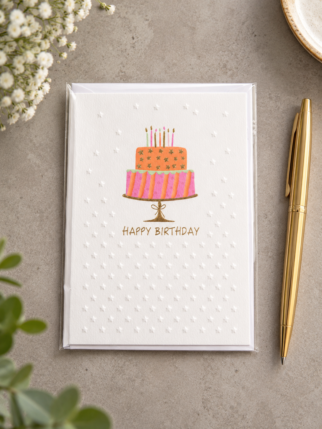 Embossed Happy Birthday greeting card featuring a two-tier birthday cake on a gold foil pedestal stand