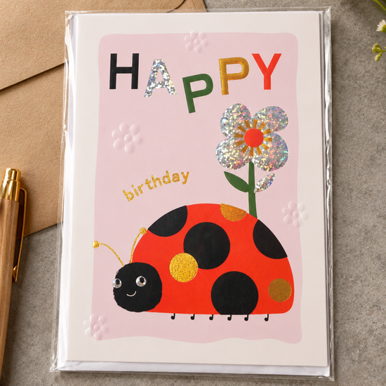 Kids Happy Birthday greeting card with smiling ladybug, googly eyes, holographic silver flower, and kraft envelope