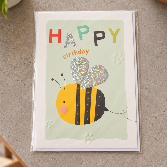 Kids Happy Birthday greeting card featuring a cheerful bumblebee with holographic glitter wings on pastel green
