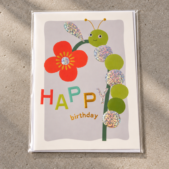 Kids Happy Birthday greeting card featuring a friendly caterpillar climbing a red flower stem with holographic circles