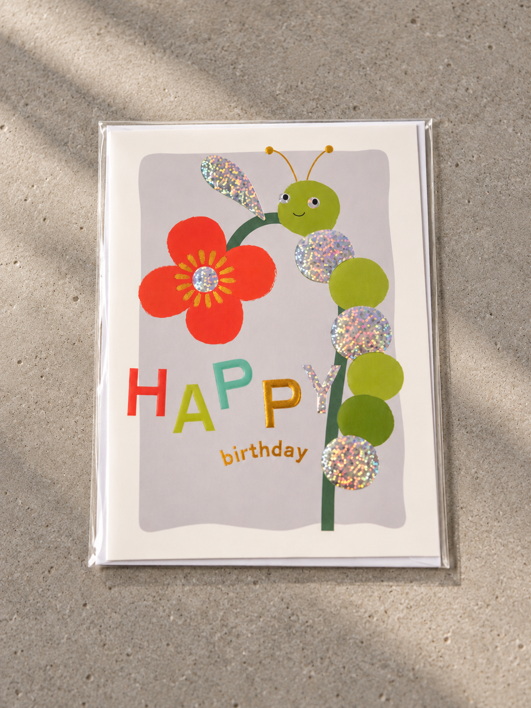 Kids Happy Birthday greeting card featuring a friendly caterpillar climbing a red flower stem with holographic circles
