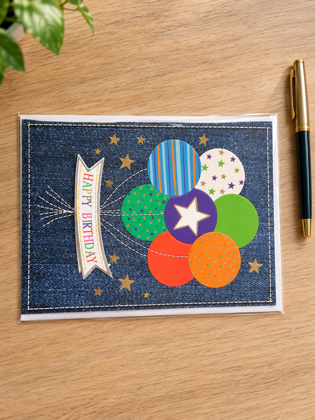 Festive denim birthday greeting card with stitched Happy Birthday banner and colorful balloon cluster