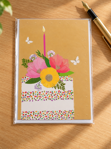 Colorful confetti sprinkle birthday cake with pink candle and floral topper on warm yellow greeting card