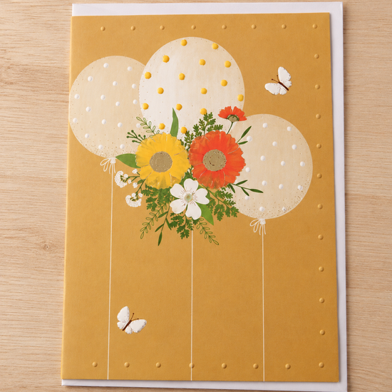 Warm yellow birthday card featuring three ivory polka-dot balloons with a vibrant floral bouquet and butterflies
