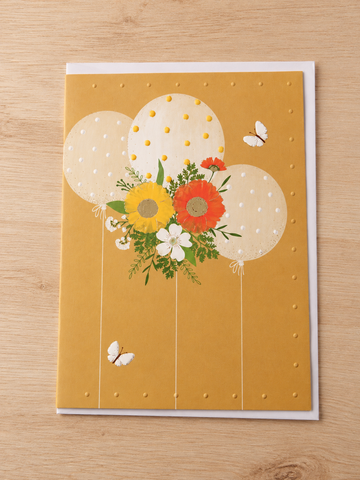 Warm yellow birthday card featuring three ivory polka-dot balloons with a vibrant floral bouquet and butterflies