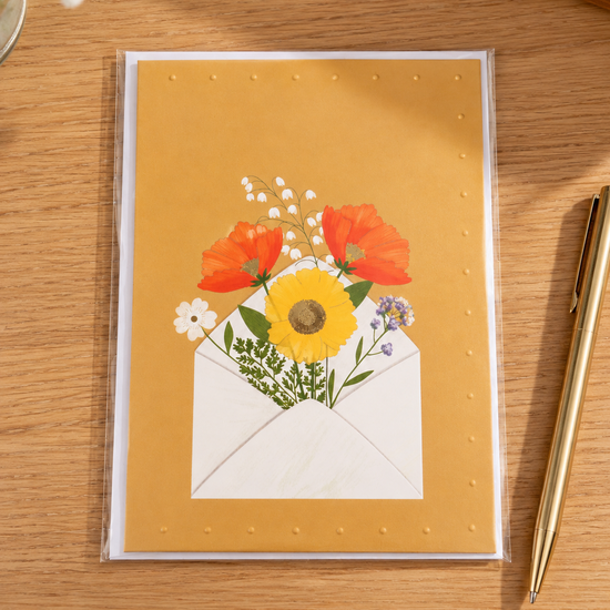 Warm yellow greeting card featuring an open white envelope overflowing with colorful wildflowers and poppies