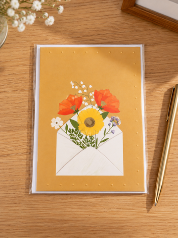 Warm yellow greeting card featuring an open white envelope overflowing with colorful wildflowers and poppies
