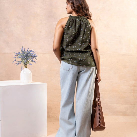 Model posing with brown shoulder bag wearing Cinnamon Isle olive green floral halter top and light jeans