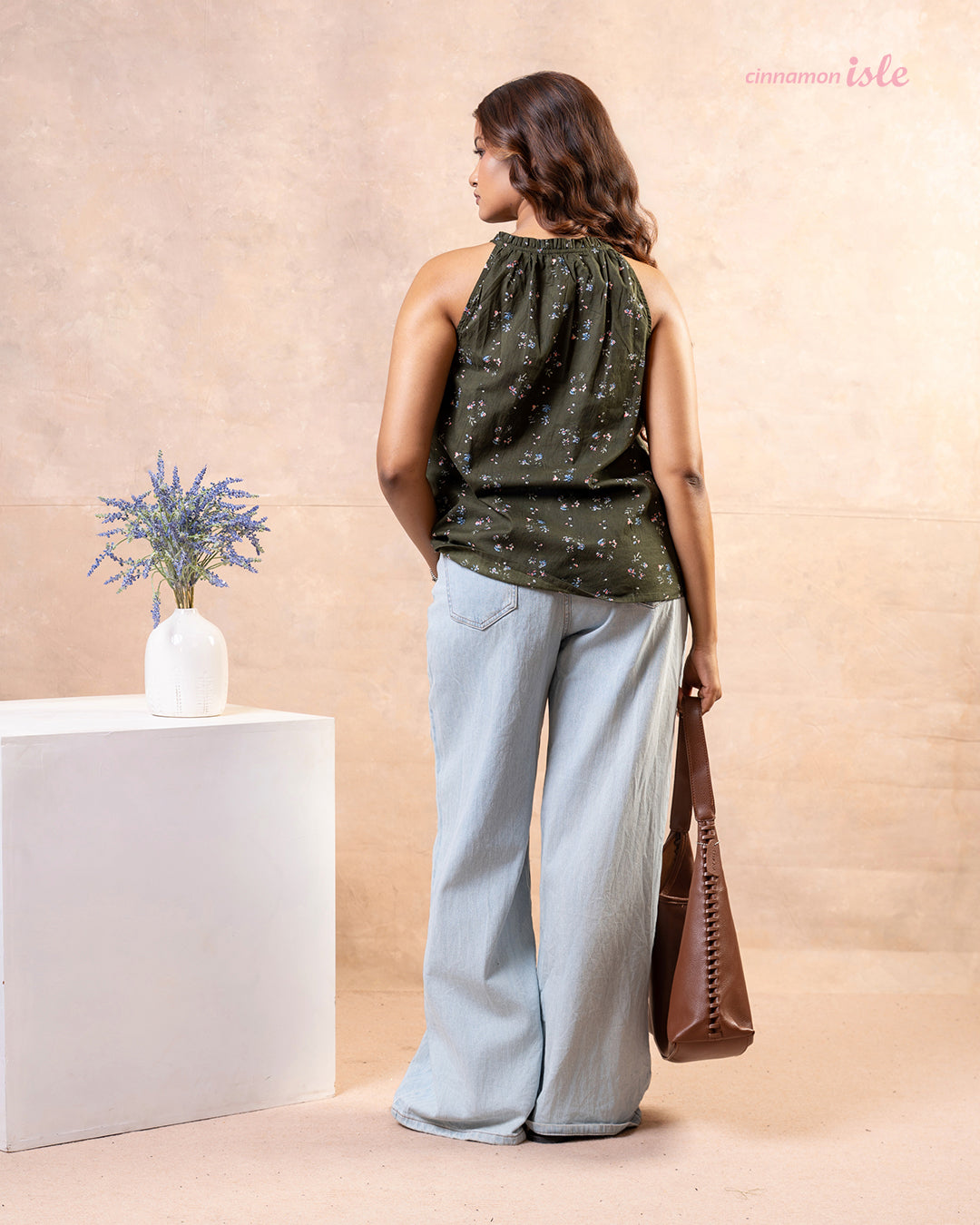 Model posing with brown shoulder bag wearing Cinnamon Isle olive green floral halter top and light jeans