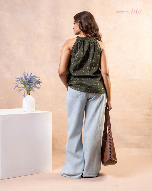 Model posing with brown shoulder bag wearing Cinnamon Isle olive green floral halter top and light jeans